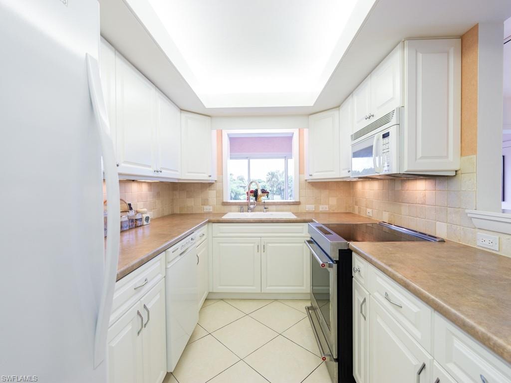 Kitchen with white appliances, a tray ceiling, light tile patterned floors, white cabinetry, and light countertops