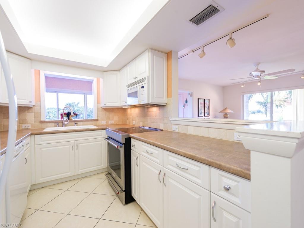 Kitchen featuring white appliances, white cabinetry, decorative backsplash, and light tile patterned floors
