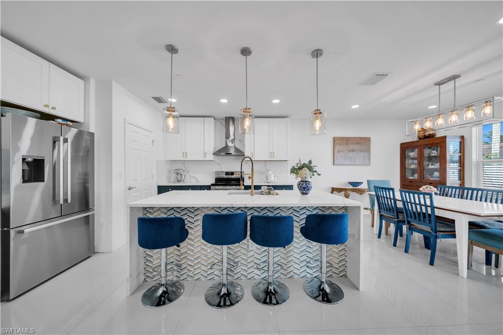 Kitchen featuring white cabinets, pendant lighting, light tile patterned floors, appliances with stainless steel finishes, and a kitchen breakfast bar