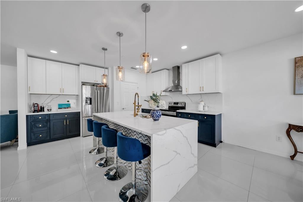 Kitchen with stainless steel appliances, light stone countertops, open floor plan, white cabinetry, and pendant lighting