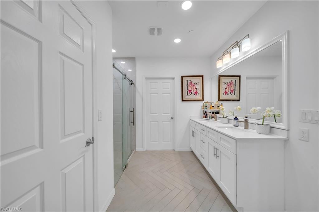 Full bathroom featuring double vanity, a marble finish shower, and recessed lighting