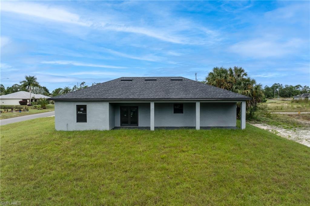Rear view of house featuring a lawn, stucco siding, and a shingled roof