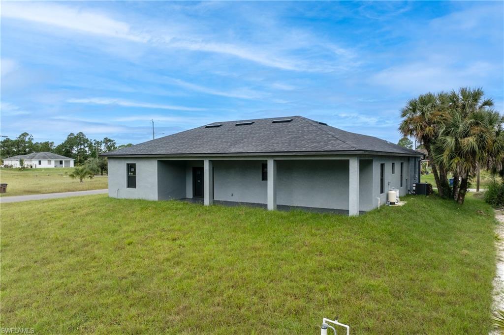 Back of property with a yard, stucco siding, and a shingled roof