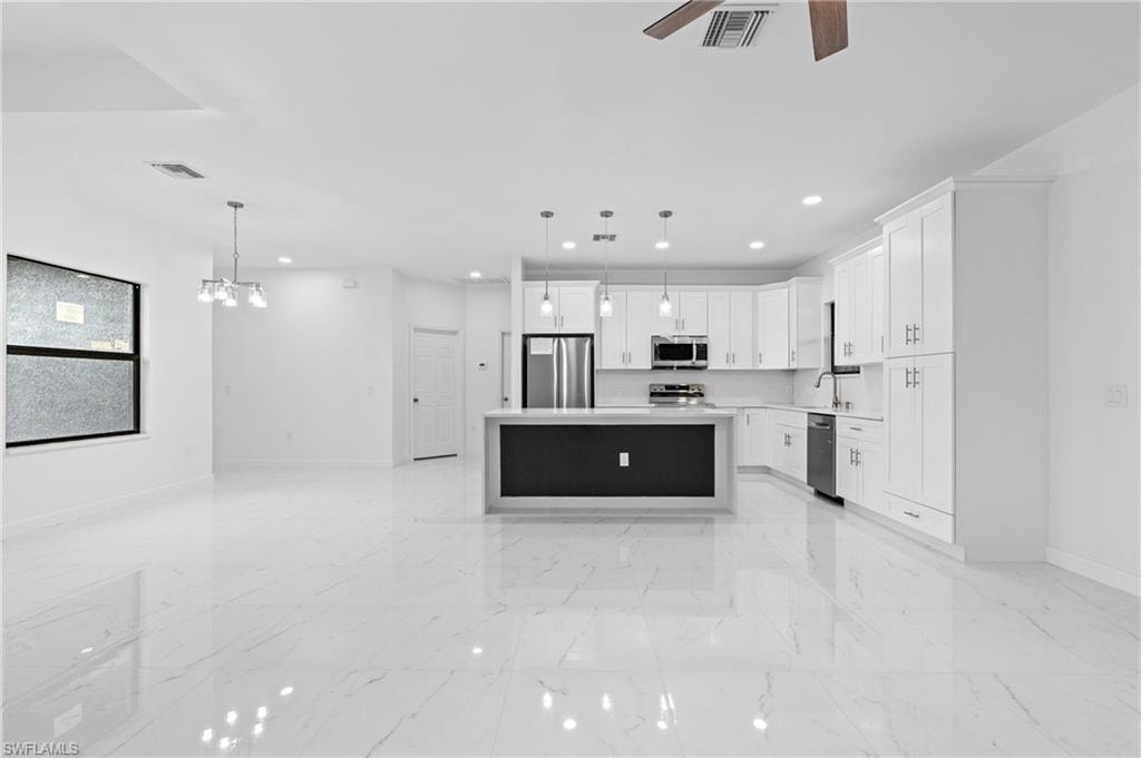 Kitchen with a kitchen island, open floor plan, white cabinetry, appliances with stainless steel finishes, and pendant lighting