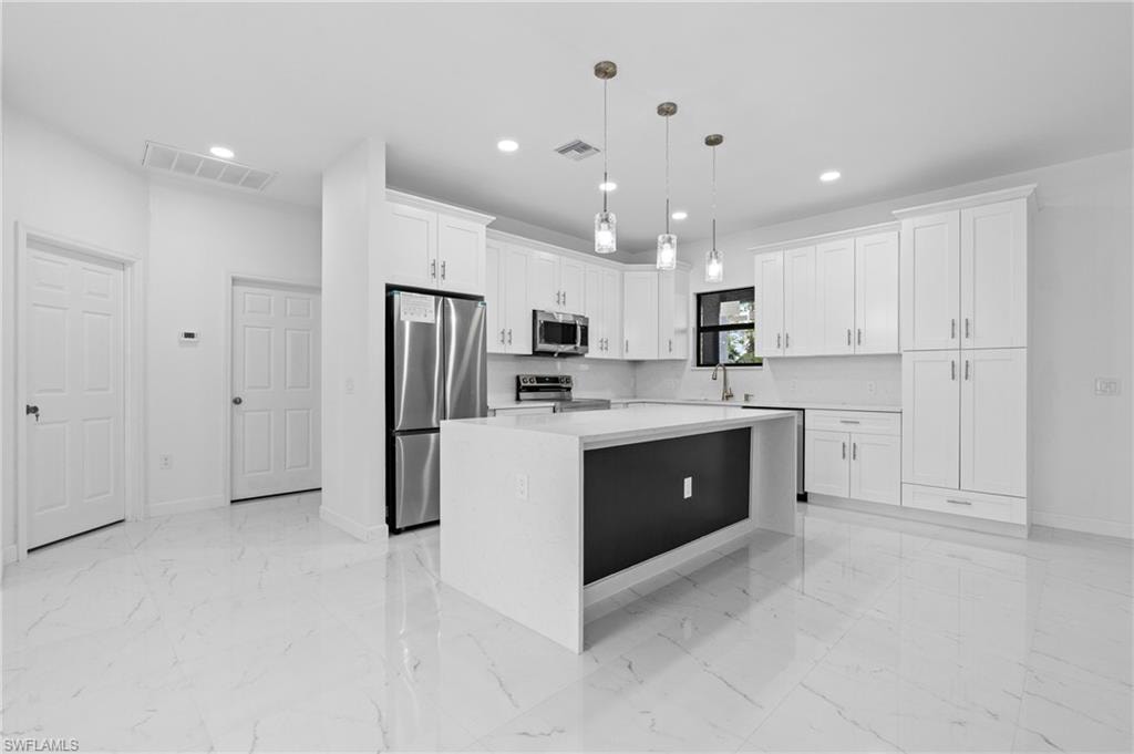 Kitchen with a kitchen island, light marble finish floors, stainless steel appliances, pendant lighting, and white cabinetry