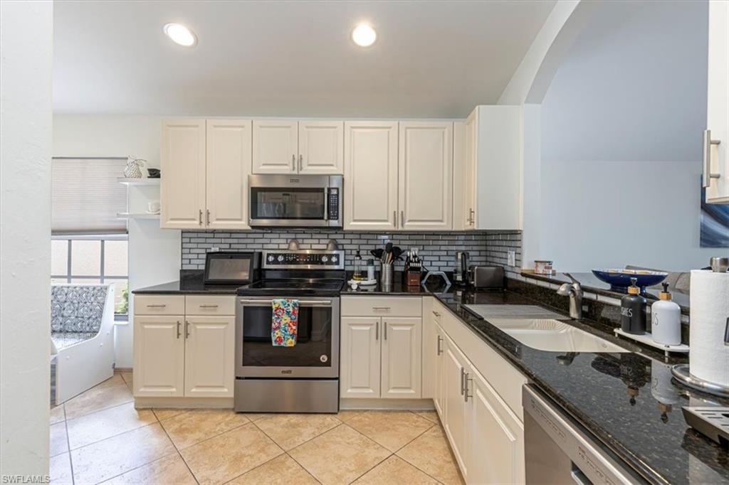 Kitchen with stainless steel appliances, decorative backsplash, dark stone countertops, light tile patterned floors, and recessed lighting