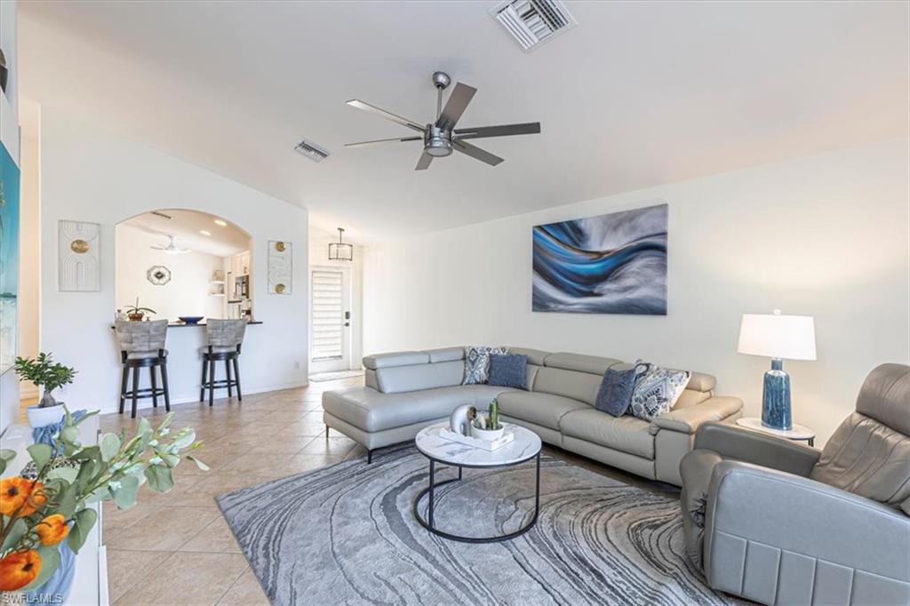 Tiled living room with a ceiling fan, arched walkways, and lofted ceiling