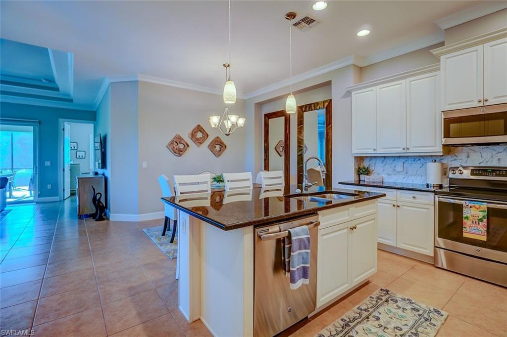 Kitchen featuring appliances with stainless steel finishes, crown molding, light tile patterned floors, backsplash, and dark stone counters