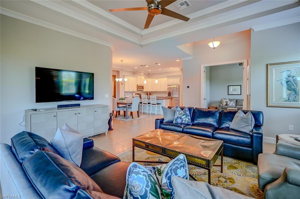 Tiled living room with a tray ceiling, crown molding, a chandelier, and a ceiling fan