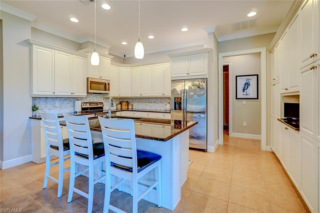 Kitchen featuring a center island with sink, stainless steel appliances, a breakfast bar area, dark stone counters, and crown molding