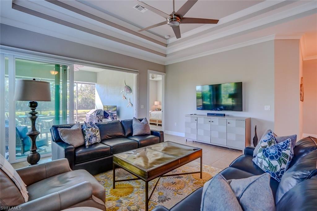 Living area with a raised ceiling, ceiling fan, light tile patterned flooring, and crown molding