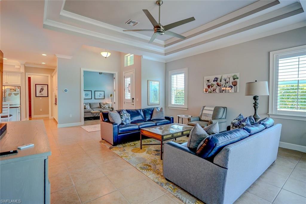 Living area with a raised ceiling, a ceiling fan, ornamental molding, and light tile patterned floors