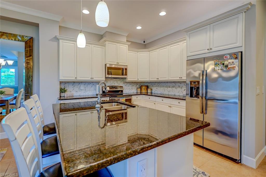Kitchen featuring light tile patterned floors, dark stone countertops, appliances with stainless steel finishes, a breakfast bar, and tasteful backsplash