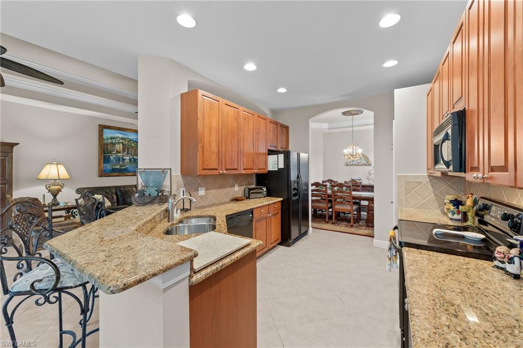 Kitchen with black appliances, light stone counters, a peninsula, hanging light fixtures, and recessed lighting
