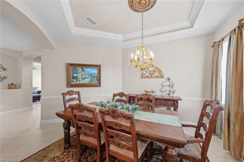 Dining space featuring arched walkways, a tray ceiling, light tile patterned floors, ornamental molding, and a chandelier