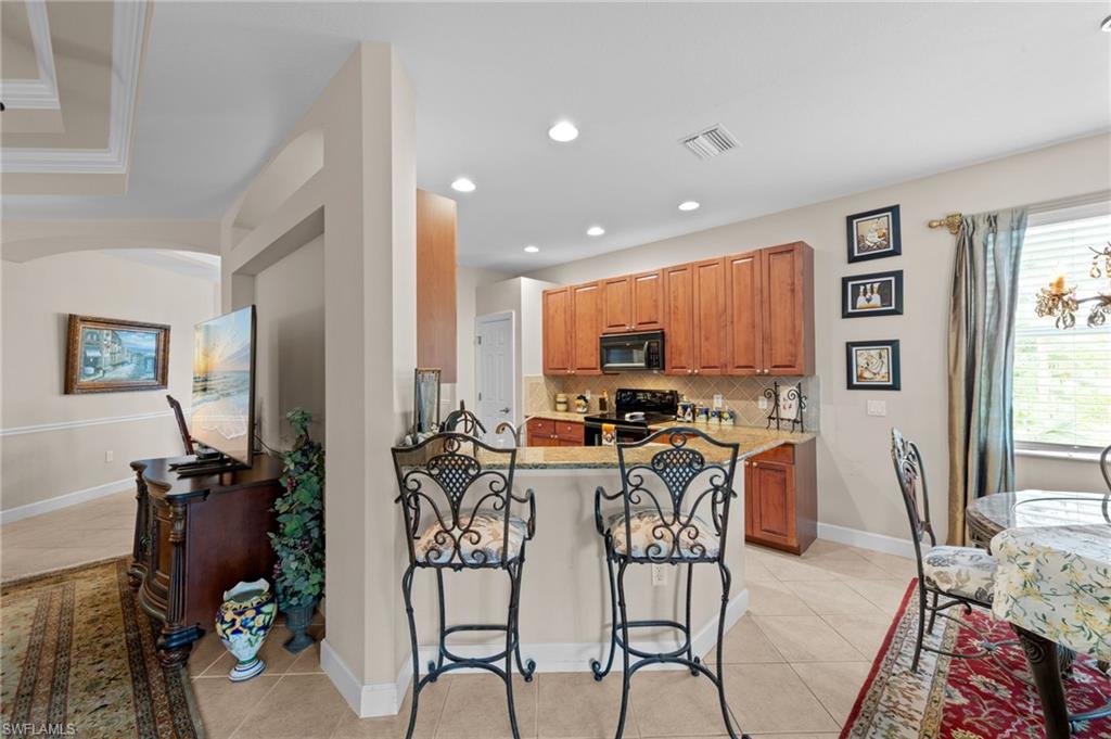 Kitchen featuring brown cabinets, light stone countertops, light tile patterned floors, a kitchen breakfast bar, and tasteful backsplash