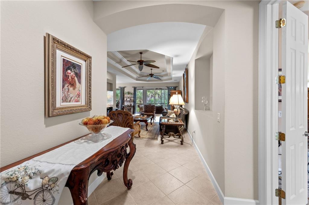 Corridor featuring a tray ceiling, light tile patterned floors, and arched walkways