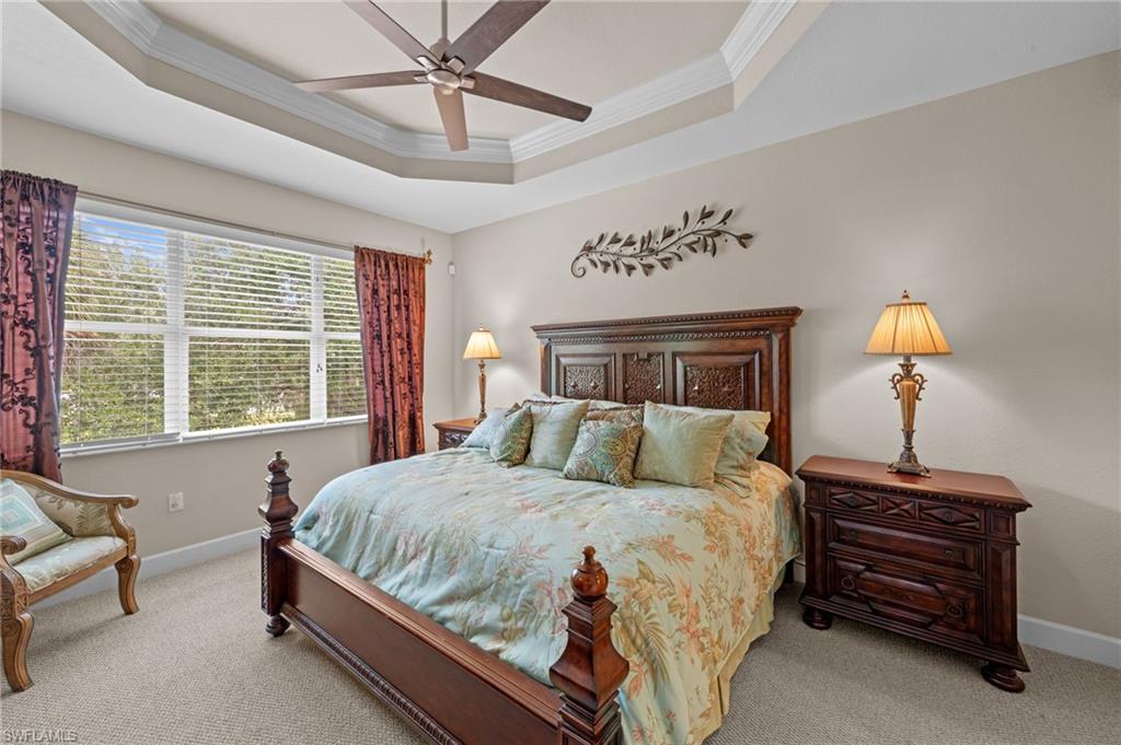 Carpeted bedroom with a tray ceiling, crown molding, and a ceiling fan