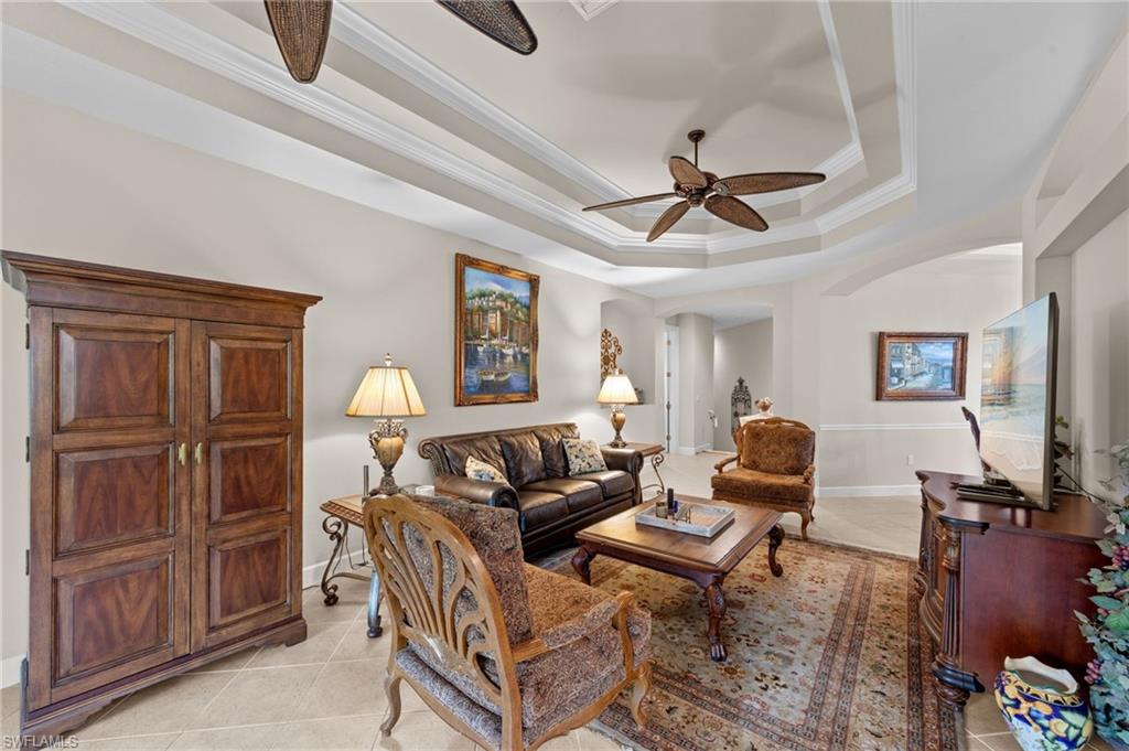 Living area with crown molding, a tray ceiling, light tile patterned floors, arched walkways, and a ceiling fan