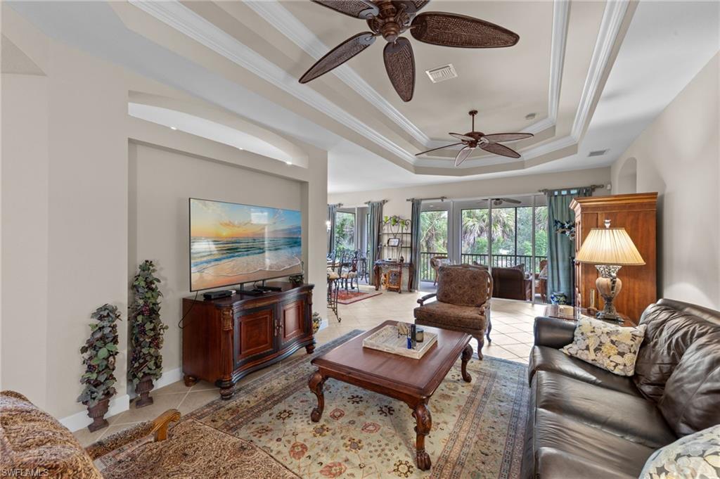 Living area with a raised ceiling, ornamental molding, light tile patterned floors, and ceiling fan