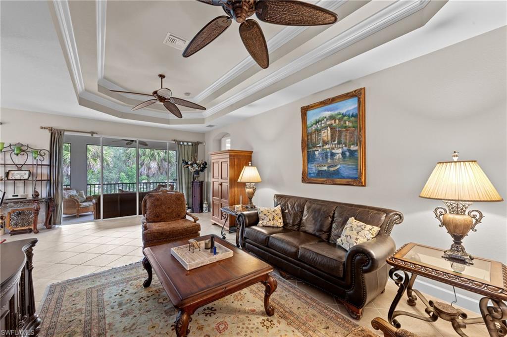 Living area with a raised ceiling, crown molding, tile patterned flooring, and ceiling fan
