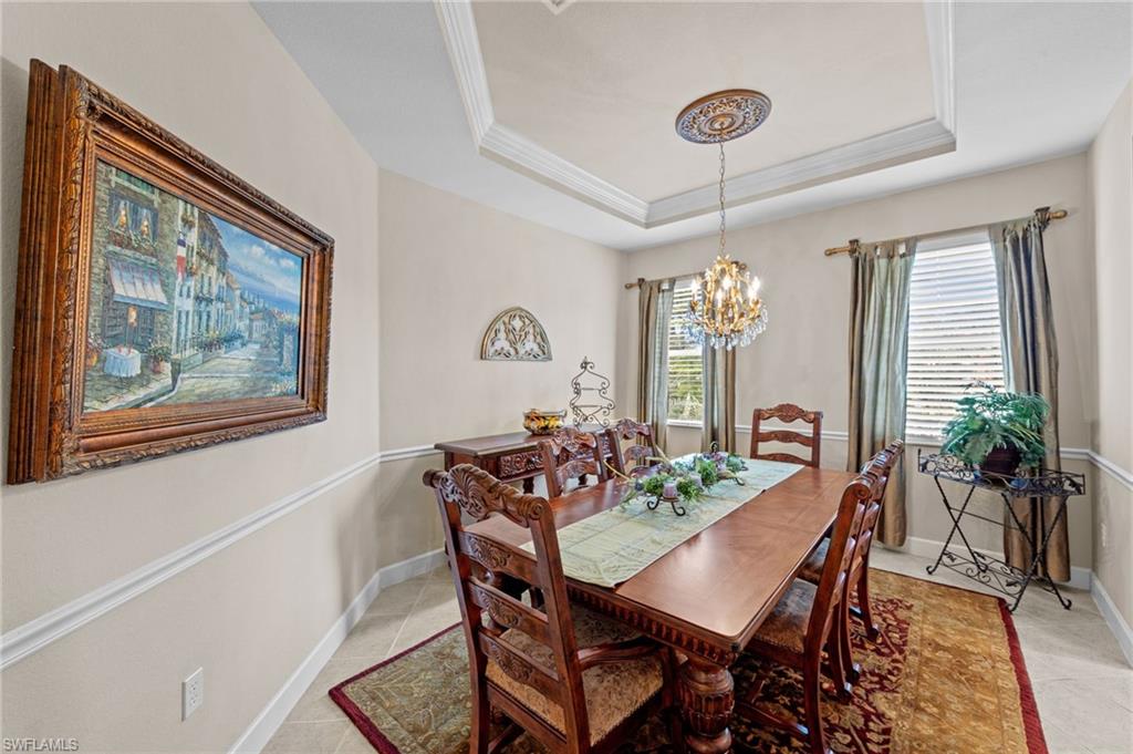 Dining space with a raised ceiling, a chandelier, ornamental molding, and light tile patterned flooring