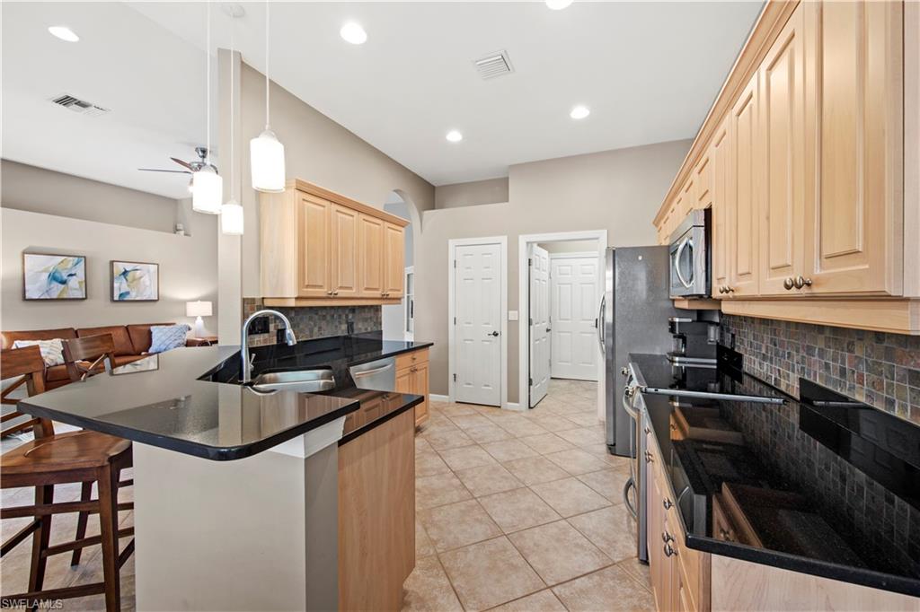 Kitchen with light brown cabinetry, decorative backsplash, a breakfast bar area, pendant lighting, and appliances with stainless steel finishes