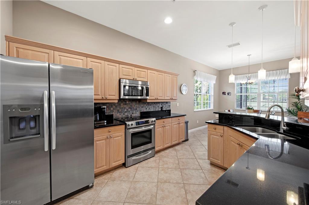 Kitchen with stainless steel appliances, light brown cabinetry, decorative light fixtures, tasteful backsplash, and light tile patterned floors