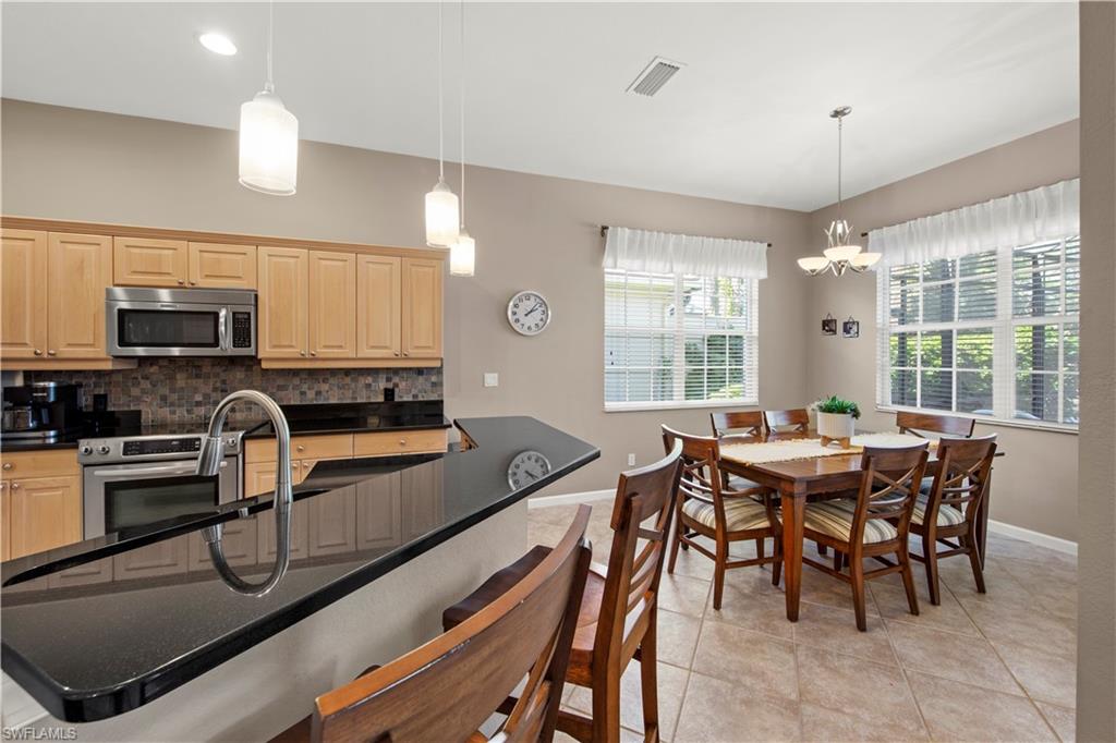 Kitchen featuring a breakfast bar, appliances with stainless steel finishes, decorative backsplash, decorative light fixtures, and light tile patterned floors