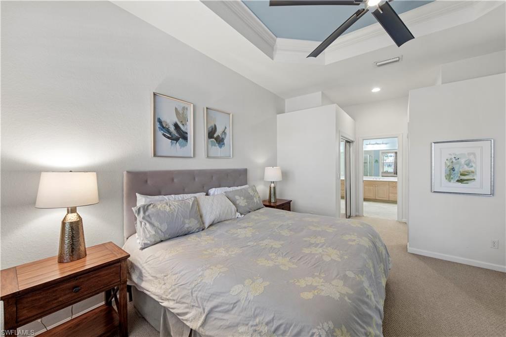 Bedroom with connected bathroom, ornamental molding, a tray ceiling, light carpet, and ceiling fan