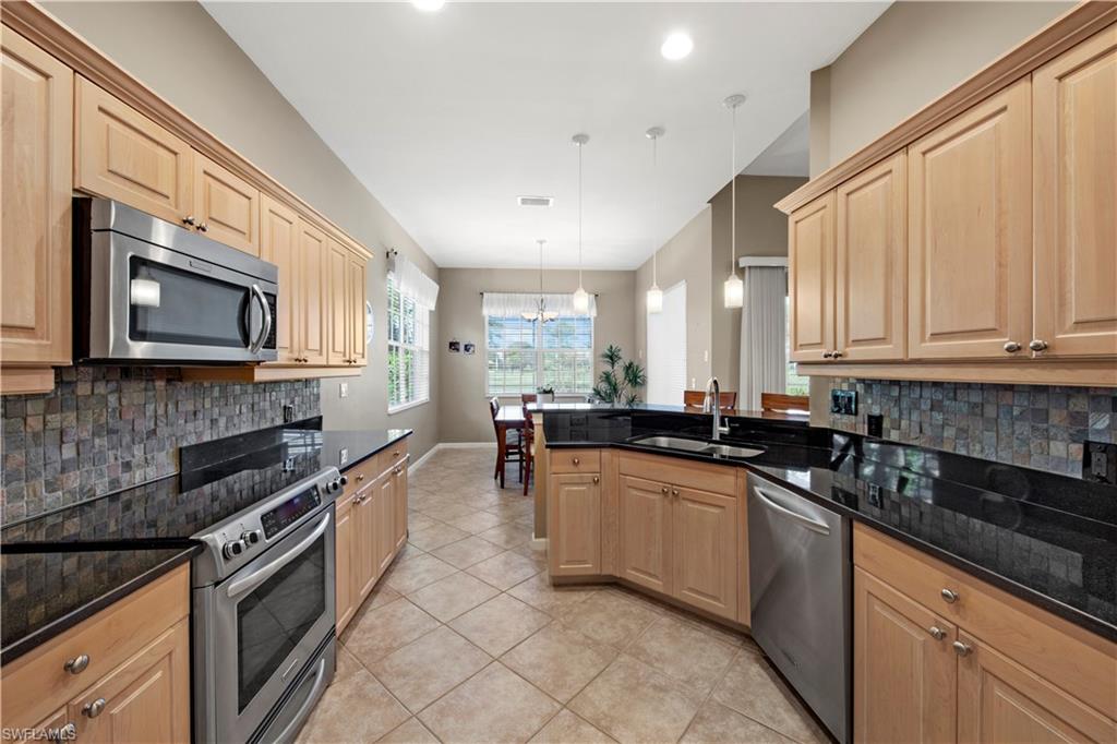 Kitchen with backsplash, appliances with stainless steel finishes, hanging light fixtures, a peninsula, and light tile patterned floors