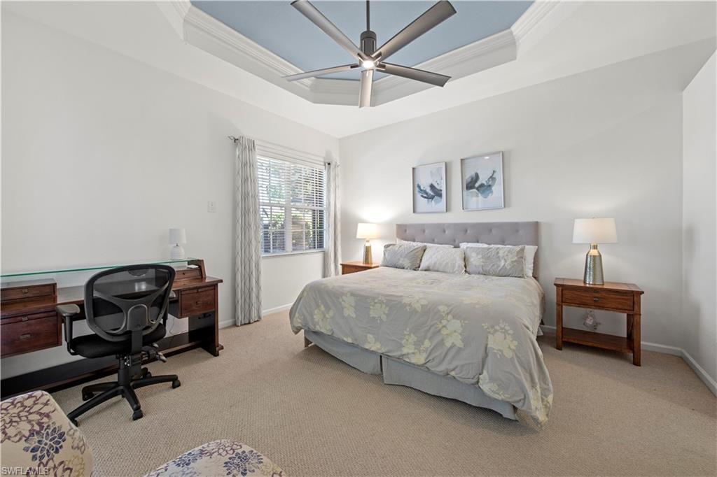 Bedroom featuring a tray ceiling, light colored carpet, crown molding, a desk, and a ceiling fan