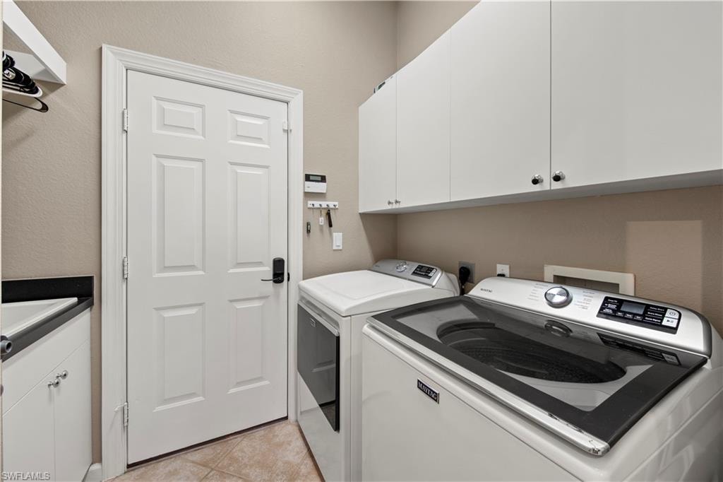 Laundry area with cabinet space, light tile patterned floors, and washer and dryer
