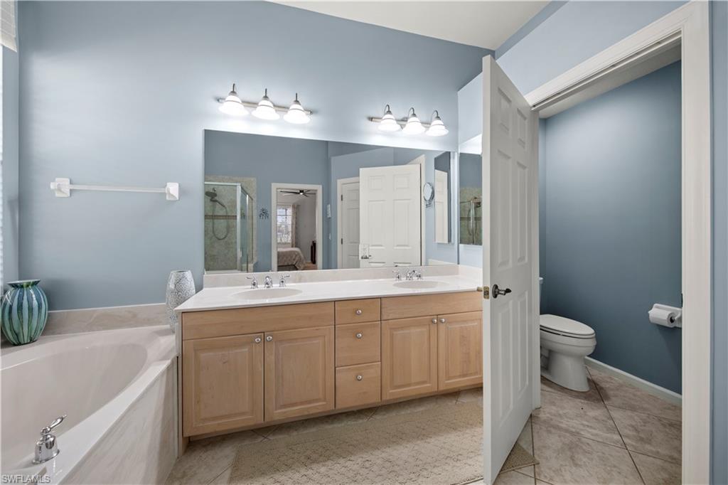 Ensuite bathroom featuring light tile patterned flooring, double vanity, a garden tub, and a stall shower