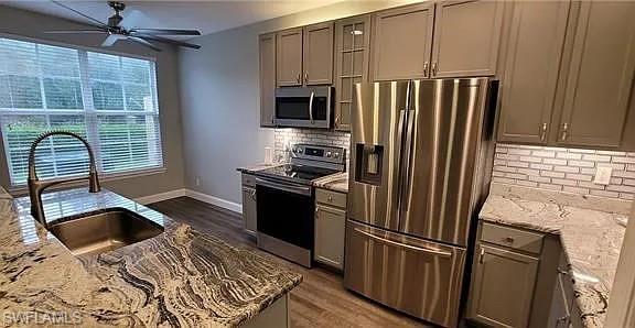 Kitchen featuring light stone counters, backsplash, stainless steel appliances, and dark wood finished floors