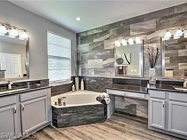 Full bath with two vanities, light wood finished floors, tile walls, a garden tub, and recessed lighting