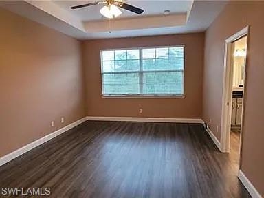 Spare room featuring a raised ceiling, dark wood-style flooring, and ceiling fan