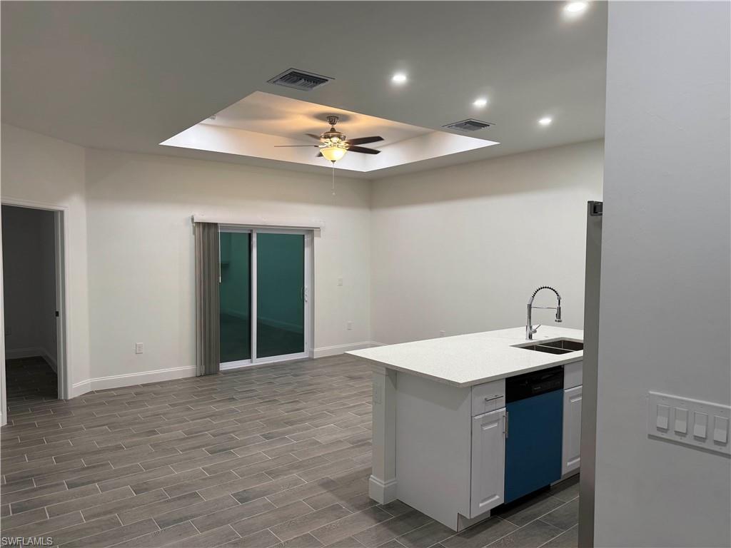 Kitchen featuring a raised ceiling, dishwashing machine, wood finish floors, white cabinets, and recessed lighting