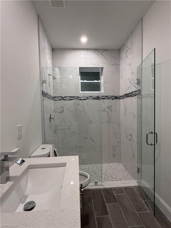 Bathroom with a marble finish shower, wood tiled floors, and vanity