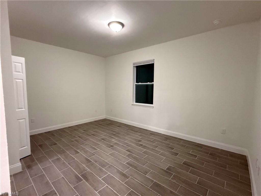 Empty room with baseboards and dark wood-type flooring