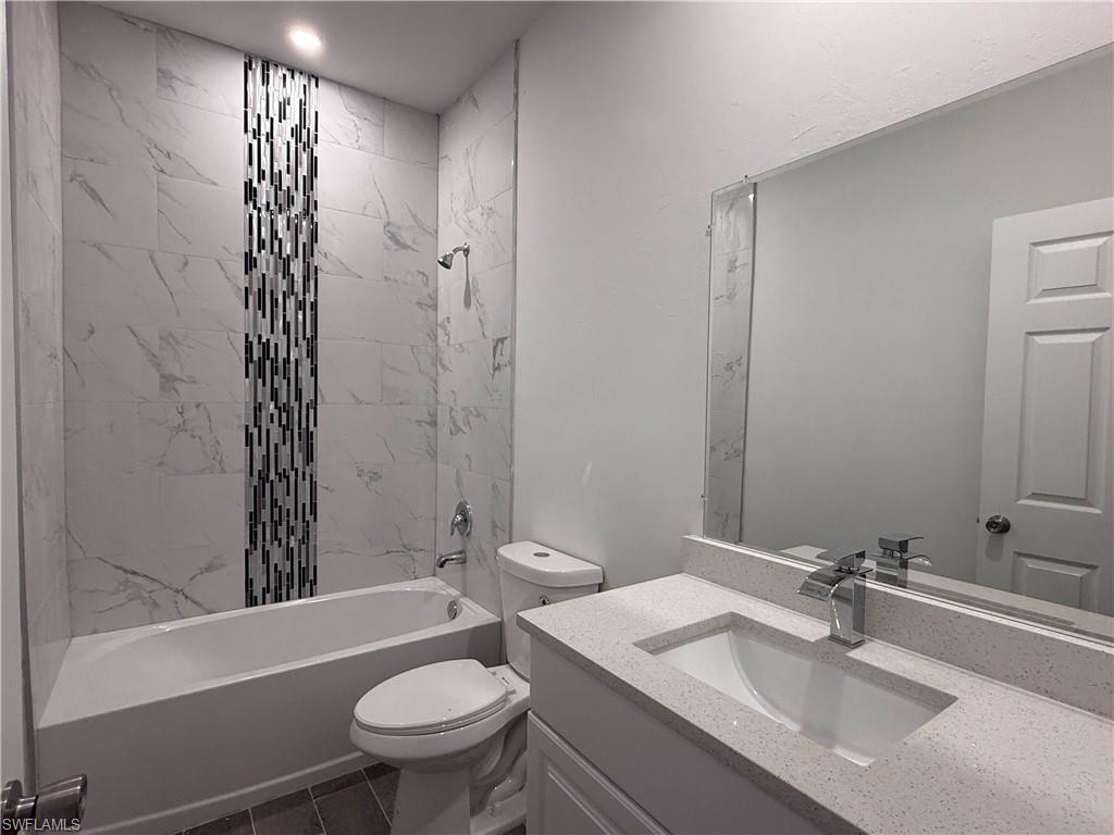 Full bath featuring vanity, washtub / shower combination, and dark tile patterned flooring