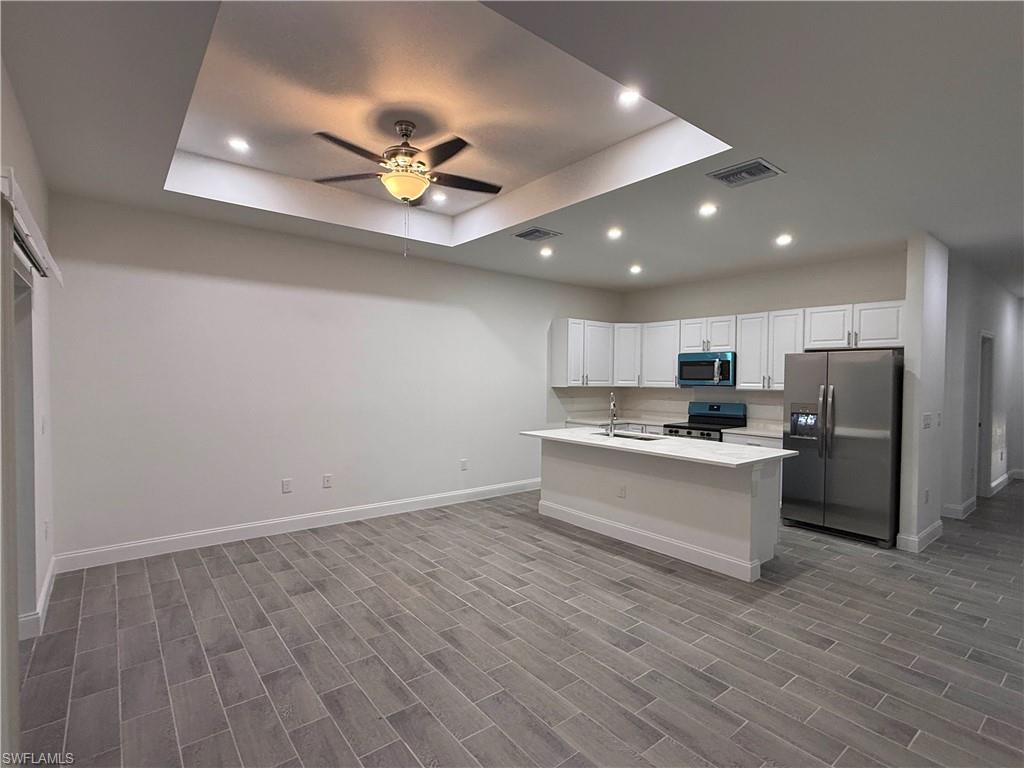 Kitchen with stainless steel appliances, recessed lighting, a raised ceiling, white cabinets, and open floor plan