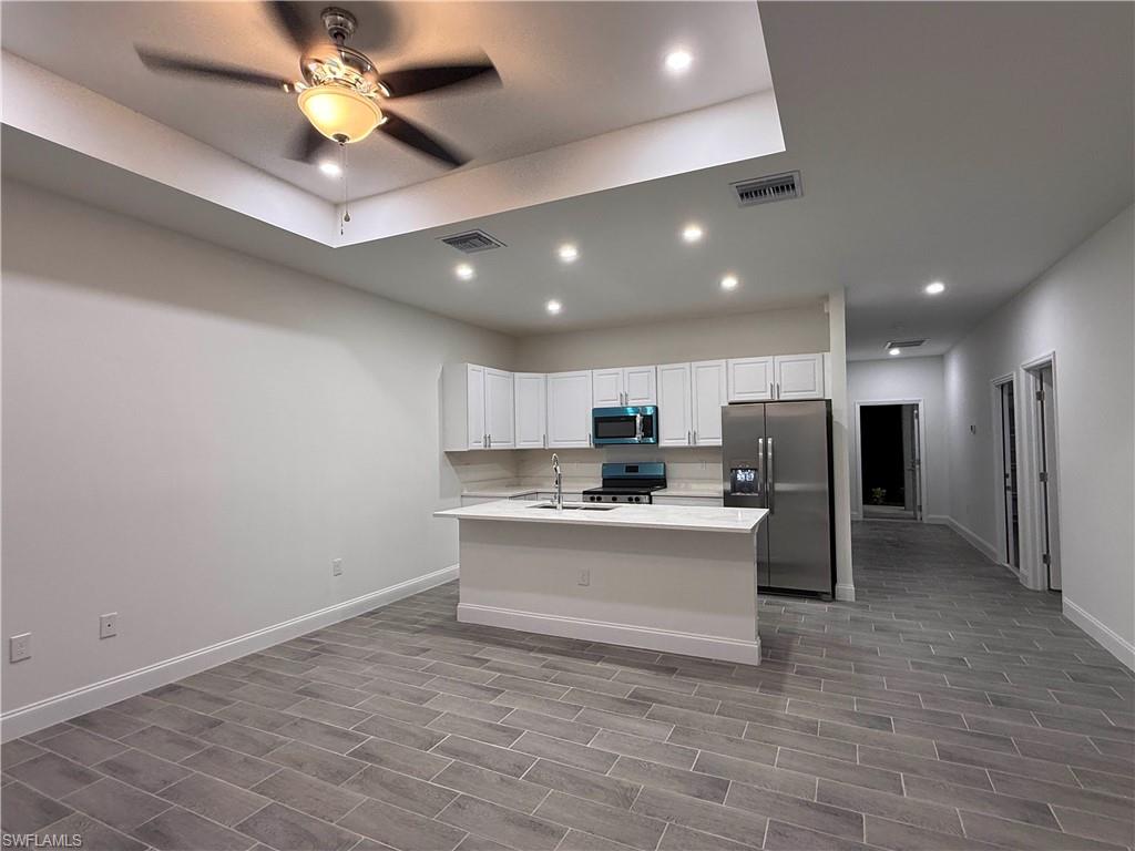 Kitchen with stainless steel appliances, recessed lighting, white cabinets, a kitchen island with sink, and wood finish floors