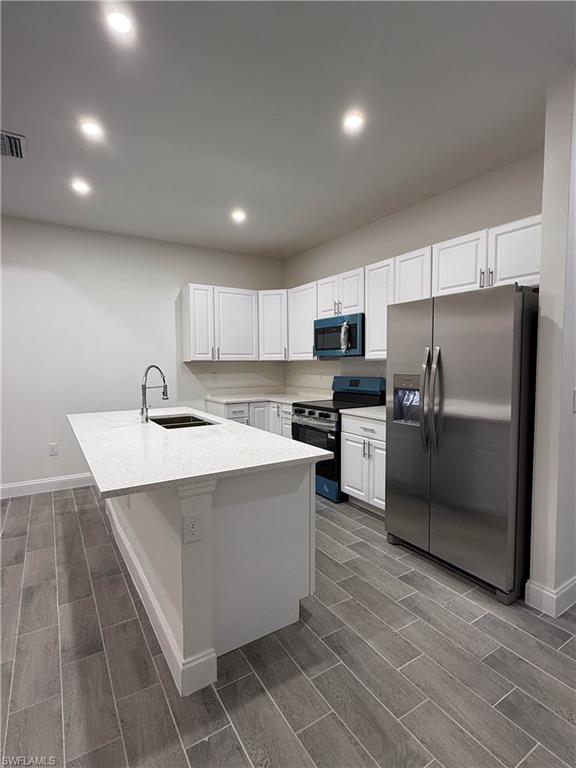 Kitchen featuring stainless steel appliances, wood tiled floors, white cabinetry, recessed lighting, and light stone counters