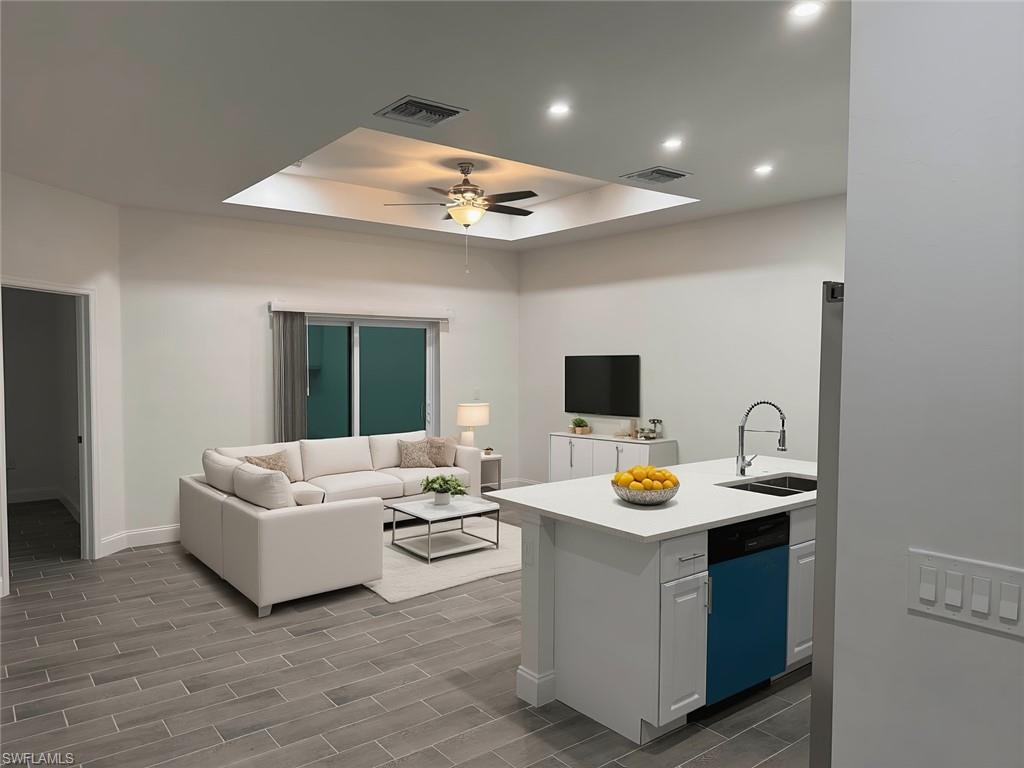 Kitchen featuring a tray ceiling, open floor plan, dishwashing machine, wood finish floors, and a peninsula