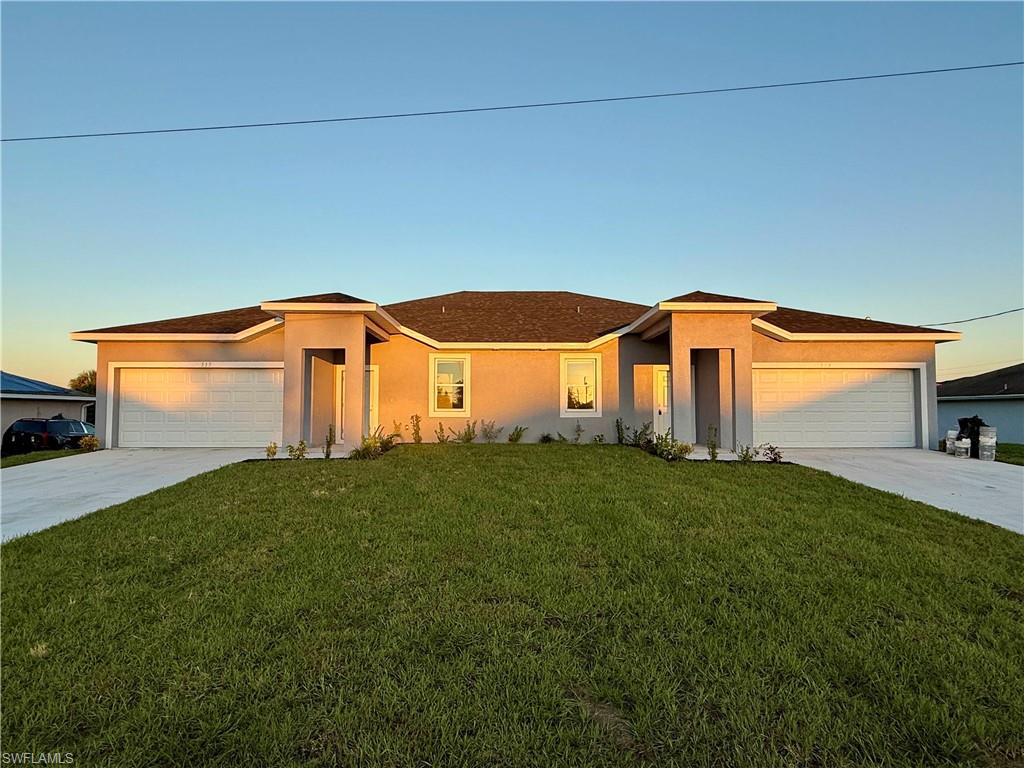 View of front of home with stucco siding, a lawn, driveway, and a garage