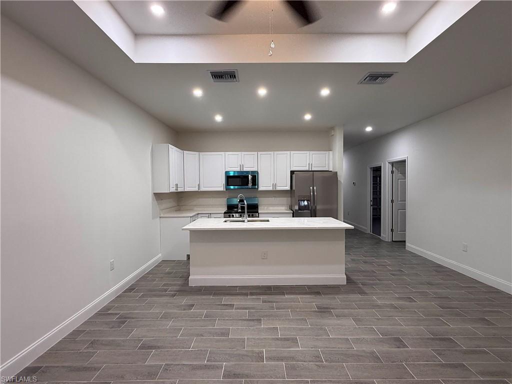 Kitchen with stainless steel appliances, a center island with sink, white cabinetry, recessed lighting, and wood finish floors