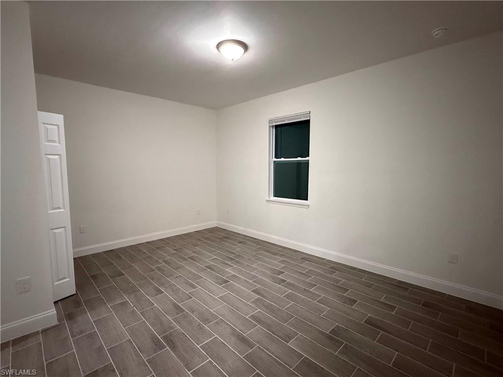 Empty room with baseboards and dark wood-type flooring