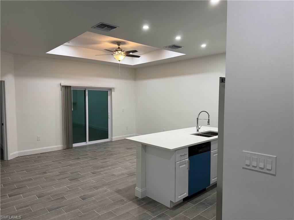 Kitchen featuring a tray ceiling, dishwashing machine, wood finish floors, white cabinets, and recessed lighting