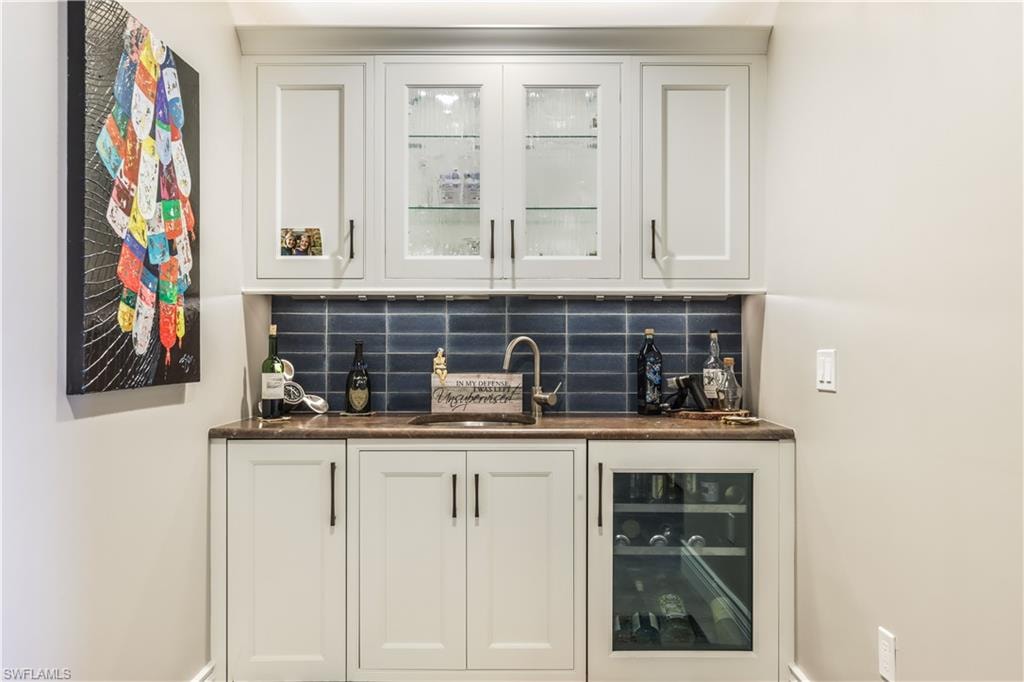 Indoor wet bar featuring white cabinetry, glass insert cabinets, and tasteful backsplash